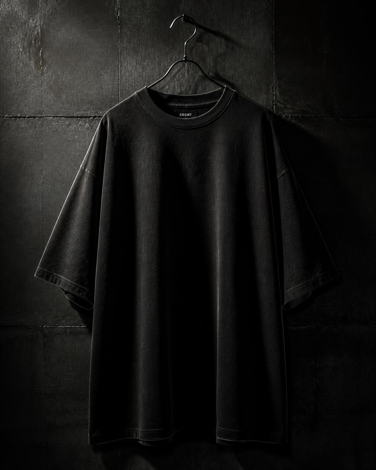 Oversized heavyweight Baseerah tee on a hanger against a dark concrete wall